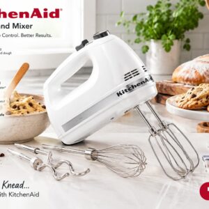 White KitchenAid 9-Speed Hand Mixer on a marble counter surrounded by baking ingredients, cookies, bread, and cupcakes